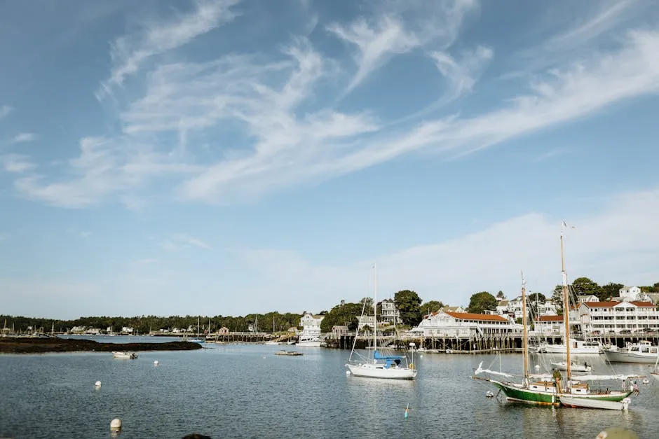 A picturesque marina in Maine with sailboats and a charming harbor town backdrop under clear skies.