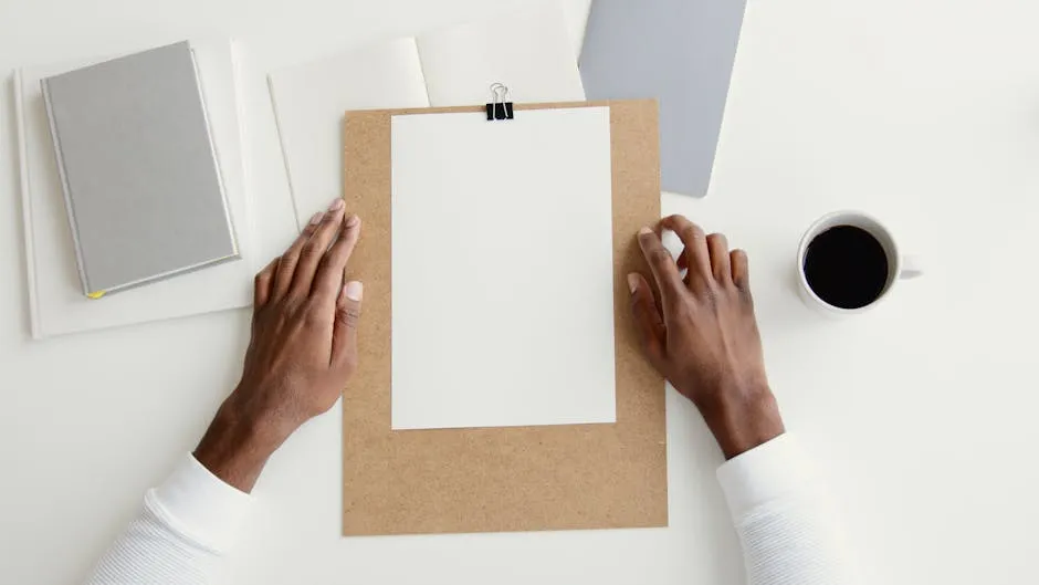 Hands holding clipboard with blank paper, notebook, and coffee on desk for creative work.