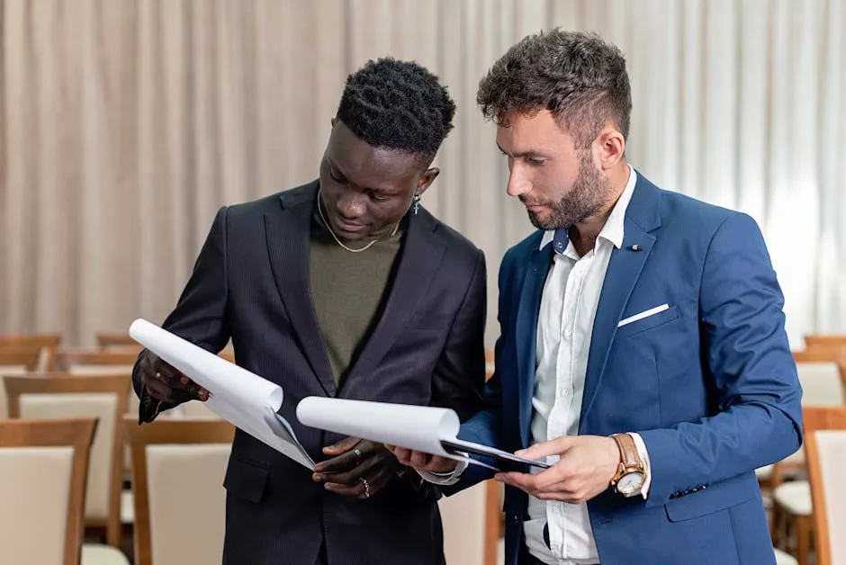 Two businessmen in suits reviewing contracts and business documents indoors.