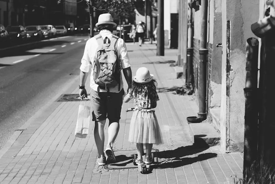 Monochrome image of a father and daughter holding hands while walking down a sunny city sidewalk.