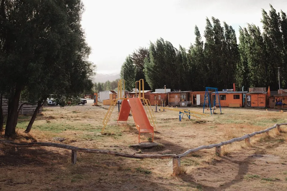 Outdoor playground set with slide and seesaws in a rural area surrounded by bungalows and trees.