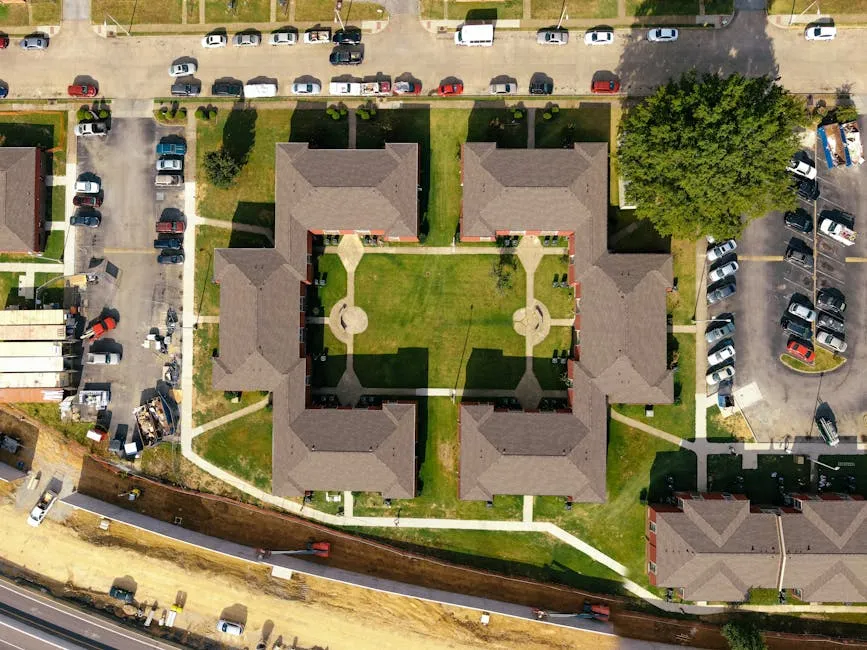 Drone view of a symmetrical apartment complex with surrounding parking areas and landscaping in a suburban setting.