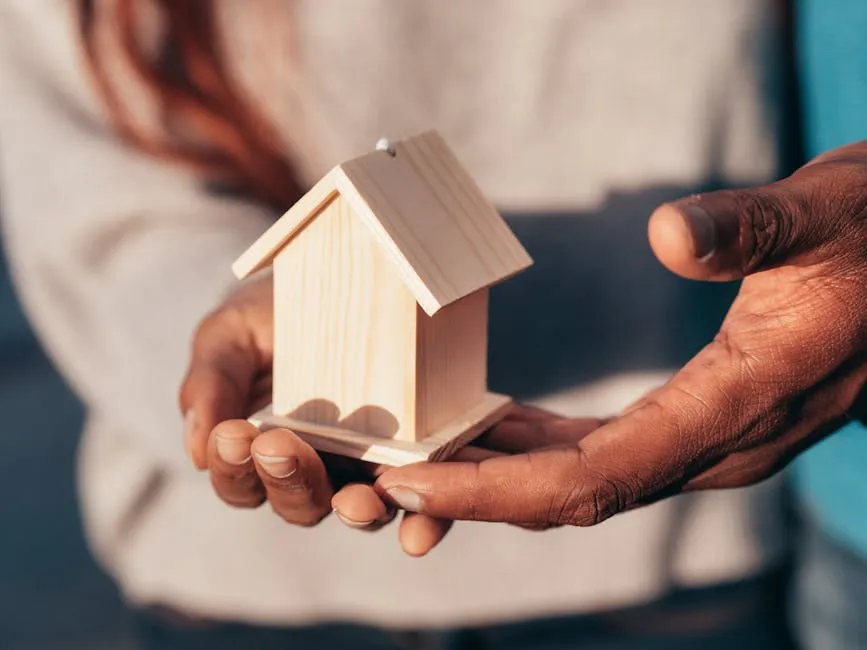 Close-up of hands holding a small wooden house, symbolizing real estate or home ownership.